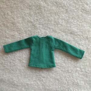 Puede incluir: Una peque&ntilde;a camiseta de manga larga de color verde esmeralda. La camiseta est&aacute; hecha de una tela texturizada y tiene cuello redondo. Las mangas son largas y llegan hasta las mu&ntilde;ecas. La camiseta est&aacute; tendida sobre una superficie blanca y texturizada.