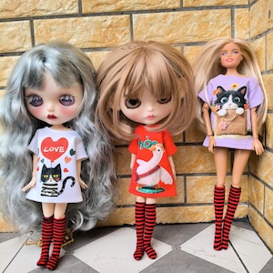 May include: Three dolls with different hairstyles and outfits. The first doll has gray hair and wears a white t-shirt with a black cat and the word "LOVE". The second doll has brown hair and a red dress with a goose design. The third doll has blonde hair and a purple dress with a cat.