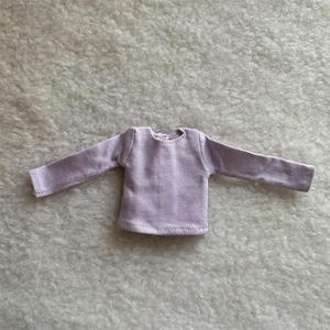 Puede incluir: Una camiseta lavanda de manga larga con textura acanalada. La camiseta tiene cuello redondo y est&aacute; hecha de una tela suave. Las mangas son largas y llegan hasta las mu&ntilde;ecas. La camiseta est&aacute; dise&ntilde;ada para una mu&ntilde;eca.
