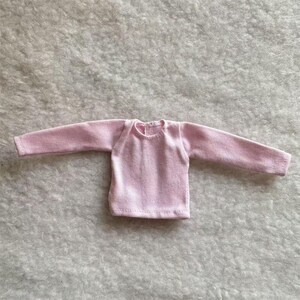 Puede incluir: Una camisa de manga larga de color rosa claro. La camisa tiene cuello redondo y est&aacute; hecha de una tela suave y texturizada. Las mangas son largas y llegan a las mu&ntilde;ecas. La camisa est&aacute; dise&ntilde;ada para una mu&ntilde;eca.