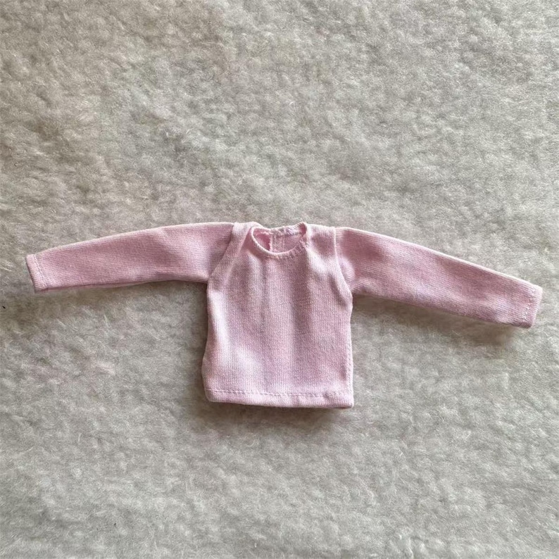 Puede incluir: Una camisa de manga larga de color rosa claro. La camisa tiene cuello redondo y est&aacute; hecha de una tela suave y texturizada. Las mangas son largas y llegan a las mu&ntilde;ecas. La camisa est&aacute; dise&ntilde;ada para una mu&ntilde;eca.
