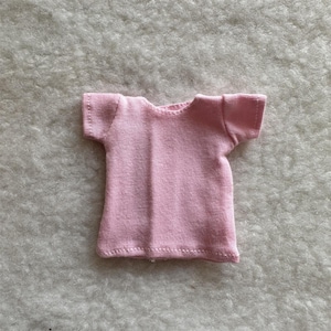 Puede incluir: Una peque&ntilde;a camiseta rosa claro con mangas cortas. La camiseta est&aacute; hecha de una tela suave y tiene un dise&ntilde;o simple y cl&aacute;sico. Las costuras son visibles, agregando un toque artesanal.