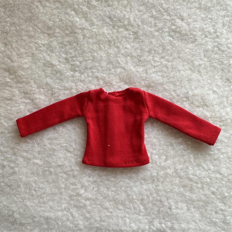 Puede incluir: Una camiseta roja brillante de manga larga. La camiseta tiene cuello redondo y est&aacute; hecha de una tela de punto suave. Las mangas son largas y terminan en pu&ntilde;os acanalados. La camiseta est&aacute; tendida sobre una superficie blanca texturizada.