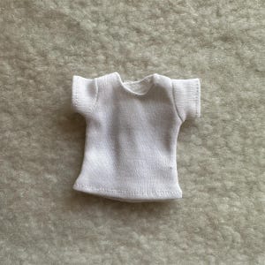 Puede incluir: Una peque&ntilde;a camiseta blanca con mangas cortas. La camiseta est&aacute; hecha de una tela suave y texturizada y tiene un cuello redondo. Las costuras son visibles y la camiseta parece nueva.