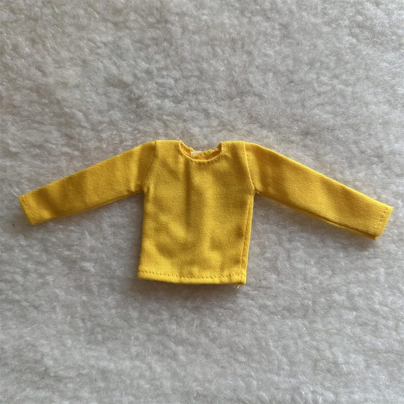 Puede incluir: Una camisa amarilla brillante de manga larga. La camisa est&aacute; hecha de una tela suave y tiene cuello redondo. Las mangas son largas y llegan hasta las mu&ntilde;ecas. La camisa est&aacute; dise&ntilde;ada para una mu&ntilde;eca.