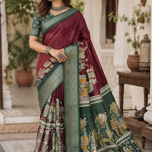May include: A maroon and dark green saree featuring a wide, ornate metallic green border and a patterned section with detailed illustrations of figures in yellow, green, and white. The blouse is dark green with a white geometric print pattern.