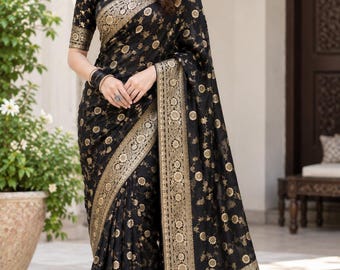 May include: A black saree featuring intricate gold floral patterns throughout the fabric. The garment includes a wide, ornate gold border with detailed motifs and a matching short-sleeved blouse, creating a cohesive and elegant ensemble.
