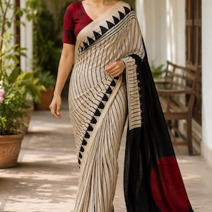 May include: A saree featuring a cream-colored base with vertical black stripes and a black triangular border pattern. The garment includes a deep red blouse with a dark floral print and a long black pallu end section featuring a large solid red circle.