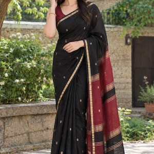 May include: A black saree featuring small gold embroidered motifs throughout the fabric, a gold border, and a wide maroon end piece with horizontal gold stripes and black tassels at the hem, paired with a sleeveless maroon blouse.