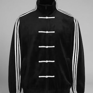 May include: Black track jacket with white stripes down the sleeves and a high collar. The jacket features white toggle closures down the front and a ribbed hem and cuffs. The jacket is made of a soft, velvety material.