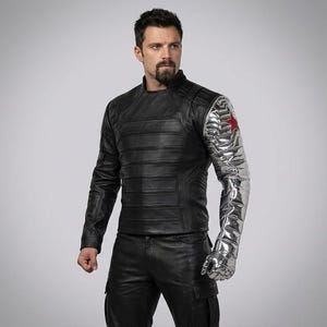 Op de afbeelding: Zwarte leren jas met horizontale stiksels en een metallic zilveren arm met een rood sterembleem. De jas heeft een opstaande kraag en wordt gecombineerd met een zwarte broek.