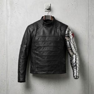 Op de afbeelding: Zwarte leren jas met een hoge kraag en een gewatteerd ontwerp. De rechter mouw is een metallic zilveren prothese met een rood sterembleem. De jas hangt aan een wandhaak tegen een grijze betonnen achtergrond.