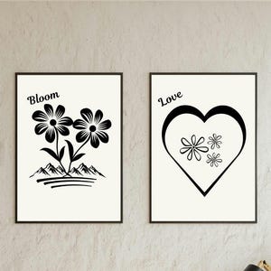 May include: Two framed wall art prints with black designs on a white background. The left print features two flowers above mountain silhouettes with the text Bloom. The right print displays a large heart outline containing three small flowers with the text Love.