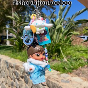 May include: A collection of keychains featuring a Bratz doll in a blue outfit, a white cartoon character, and other charms. The keychains are attached to a silver chain. The text "@shopbijoubooboo" is visible.