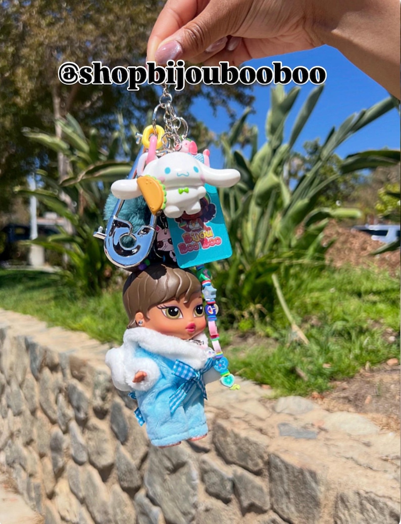 May include: A collection of keychains featuring a Bratz doll in a blue outfit, a white cartoon character, and other charms. The keychains are attached to a silver chain. The text "@shopbijoubooboo" is visible.