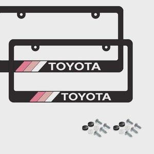May include: Two black license plate frames with the word "TOYOTA" in white. The frames have a pink, white, and pink stripe design. Mounting hardware is included. Automotive accessories.