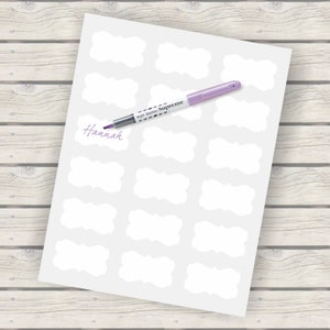 May include: A sheet of white paper with 20 blank, white, scalloped labels. A purple highlighter pen is lying on top of the paper with the word "Supreme" written on the side of the pen. The word "Hannah" is written in purple ink on the paper.
