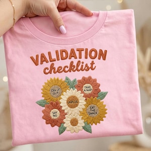 Puede incluir: Camiseta rosa claro con la inscripción bordada "VALIDATION checklist" sobre un diseño floral. Las flores incluyen las frases "CRY IT OUT", "TAKE A NAP", "EAT THE SNACK", "SAY NO" y "UNPLUG".