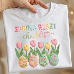 May include: White crew neck sweatshirt with embroidered text "SPRING RESET checklist". Below the text are embroidered tulips and Easter eggs with phrases like "BLOOM" and "EAT CHOCOLATE".