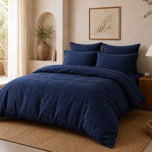Peut inclure: Un ensemble de literie bleu marine comprenant une housse de couette et des taies d'oreiller. La literie est sur un lit avec un tapis tissé. Une table de chevet en bois avec une lampe et un tableau encadré sont également dans la pièce.
