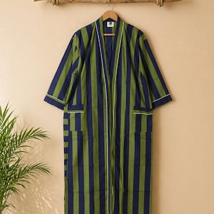 May include: A long, striped robe in shades of navy blue and olive green, hanging on a wooden hanger. The robe features vertical stripes, white trim, and two front pockets. The robe is displayed against a neutral background.