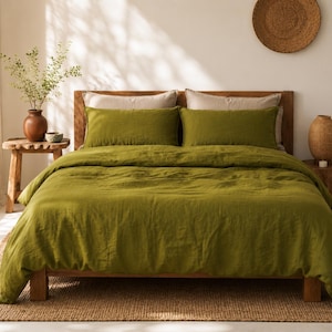 May include: A bed featuring a solid olive green duvet cover and two matching rectangular pillow shams. Behind these are two neutral beige pillows. The bed frame is constructed from wood and sits on a woven rug, creating a cohesive bedding set.