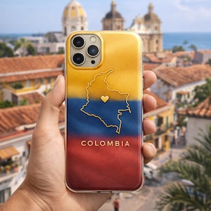 May include: A smartphone case with a yellow, blue, and red gradient design. It features a gold outline of Colombia's map and a heart. The word "COLOMBIA" is printed at the bottom. The case is held in front of a blurred cityscape.