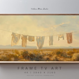 May include: A framed digital art print depicts laundry hanging on a clothesline in a desert landscape. The artwork features a warm color palette with beige and peach tones, and the text "Verbena Bloom Studio" is visible.