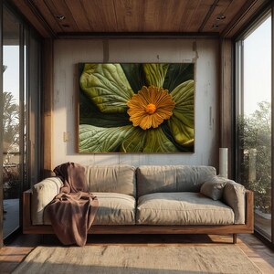 May include: A large framed artwork featuring a close-up of a yellow flower with a textured center, set against large green leaves. The artwork hangs above a neutral-toned sofa with a brown throw blanket. The room has wooden accents and large windows.