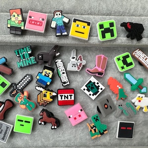 May include: A collection of colourful rubber shoe charms featuring various pixelated characters, tools, animals, and items from the Minecraft video game, including a pig, creeper, sword, TNT block, and the Minecraft logo, all with a flat, matte finish.