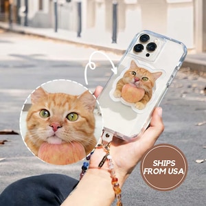 May include: Clear phone case with a sticker of an orange tabby cat holding a peach. The case has a wrist strap with colorful beads. The image also includes a close-up of the cat's face.