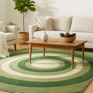 Könnte beinhalten: Wohnzimmer mit einem grünen und cremefarbenen kreisförmigen Teppich. Ein Holztisch mit einer Holzschale mit Tannenzapfen und einer weißen Vase. Ein beiges Sofa und ein Sessel im Hintergrund, mit einer Topfpflanze links.