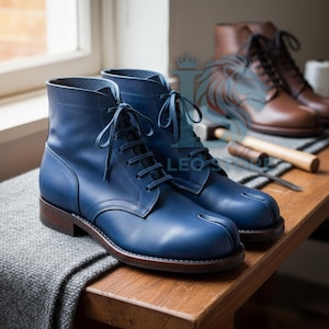 May include: A pair of blue leather boots with a lace-up design, featuring a split-toe detail. The boots have a dark brown sole and heel. Additional brown boots are visible in the background, along with tools on a wooden surface.