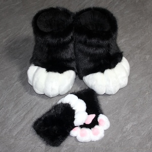 May include: Black and white faux fur paw-shaped slippers and matching hand covers. The slippers have a black upper and white paw pads. The hand covers have black fur with white paw pads and pink toe pads. The items are designed to resemble animal paws.