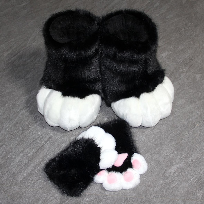May include: Black and white faux fur paw-shaped slippers and matching hand covers. The slippers have a black upper and white paw pads. The hand covers have black fur with white paw pads and pink toe pads. The items are designed to resemble animal paws.