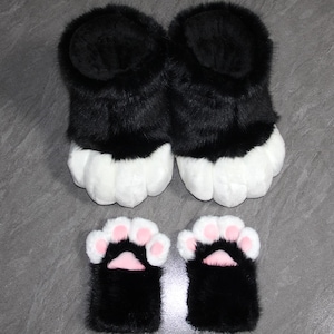 May include: A set of black and white furry paw slippers and matching paw mittens. The slippers and mittens have white paw pads with pink accents. The faux fur is black and white.