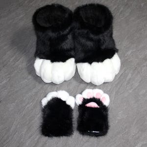 May include: Black and white furry paw slippers and matching hand covers. The slippers have a black upper and white paw pads. The hand covers are black with white and pink accents.