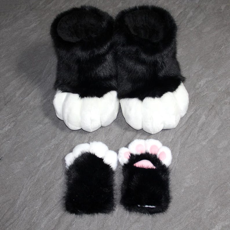 May include: Black and white furry paw slippers and matching hand covers. The slippers have a black upper and white paw pads. The hand covers are black with white and pink accents.