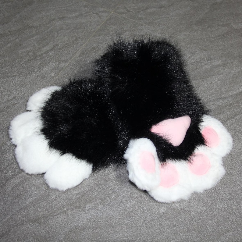 May include: A pair of plush black and white cat paw gloves. The gloves have white fur on the paws with pink paw pads. The top of the gloves are black and fluffy.