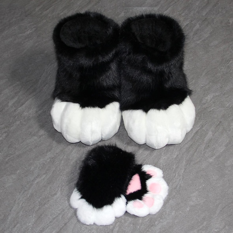 May include: A pair of black and white furry paw-shaped slippers with matching paw-shaped hand covers. The slippers and hand covers have a black upper portion and white paw pads. The hand covers have pink paw pads.