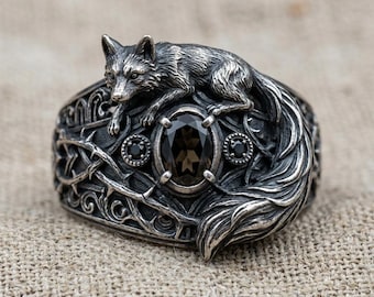 May include: A silver-toned ring featuring a detailed fox design. The ring has an oval, dark gemstone at the center, flanked by smaller black stones. The band is intricately carved with a thorn and vine pattern, creating a gothic or fantasy aesthetic.