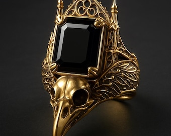 May include: A gold-colored ring featuring a large, rectangular black gemstone. The ring's design incorporates a bird skull and ornate, gothic-style detailing, with a crown-like structure above the gemstone. The ring is set against a dark background.