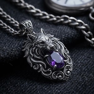 Può includere: Un ciondolo color argento con una scultura dettagliata di testa di lupo e intricati motivi a volute. Il lupo tiene in bocca una gemma sfaccettata di forma ovale color viola intenso. Il ciondolo è fissato a una spessa catena color argento.