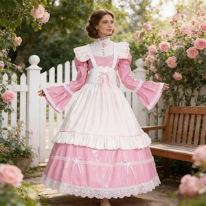 May include: A pink and white dress with a high collar, long sleeves, and a layered skirt. The dress features a white bodice with a corset-style waist and is trimmed with lace and bows. The sleeves have a flared design. The background includes a white picket fence and rose bushes.