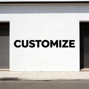 May include: A white wall with the word "CUSTOMIZE" in large, bold, black letters. The wall has two dark, closed garage doors on either side. A sidewalk and street are in the foreground.