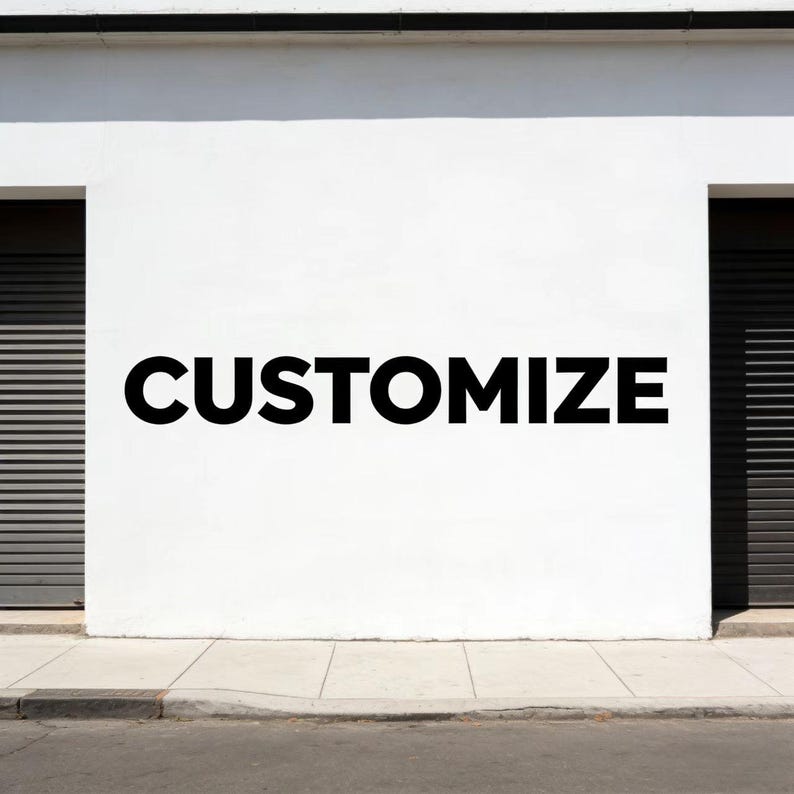 May include: A white wall with the word "CUSTOMIZE" in large, bold, black letters. The wall has two dark, closed garage doors on either side. A sidewalk and street are in the foreground.