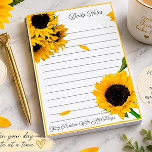 Könnte beinhalten: Ein rechteckiger Notizblock mit weißem Papier und horizontalen schwarzen Linien, verziert mit gelben Sonnenblumenillustrationen in der oberen linken und unteren rechten Ecke. Der Text lautet Daily Notes oben und Stay Positive With All Things unten.