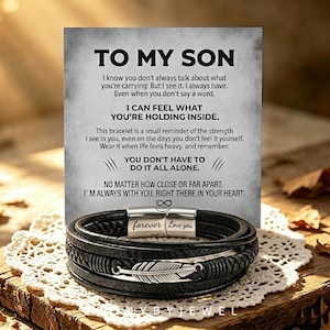 May include: A black multi-strand leather bracelet featuring a silver-toned metal feather charm and a magnetic clasp engraved with the words forever Love you. The bracelet is displayed in front of a card with the printed text TO MY SON.