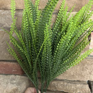 May include: A bunch of artificial fern stems featuring multiple long, slender branches covered in small, vibrant green leaves. The foliage is arranged in a dense cluster, showcasing a realistic texture and a bright, consistent green color throughout.