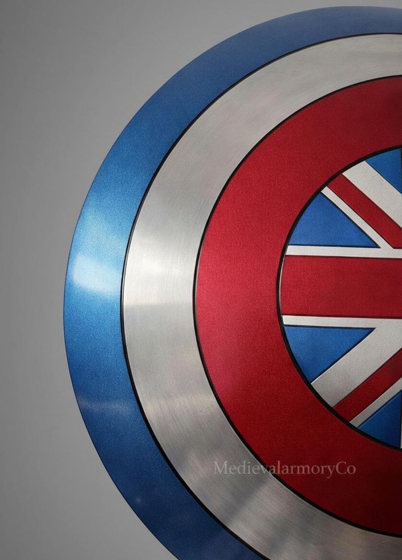 Op de afbeelding: Een close-up van een schild met een blauw, zilver en rood kleurenschema. Het schild heeft een Union Jack-ontwerp in het midden, met een blauwe buitenring, een zilveren middenring en een rode binnenring.